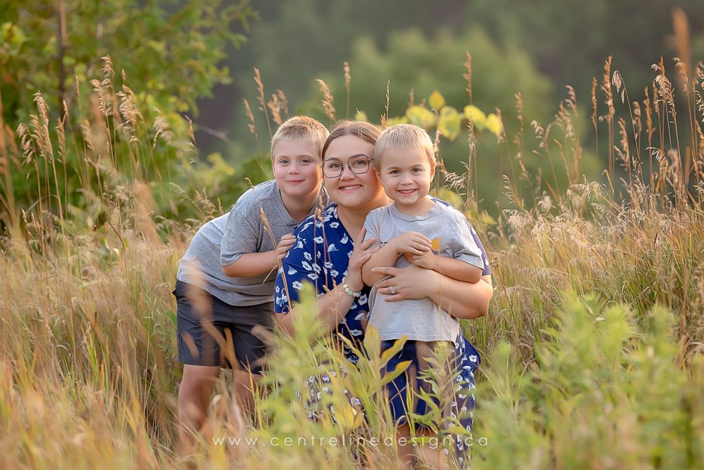 Mother cuddle with her two boys outdoor with long grass.